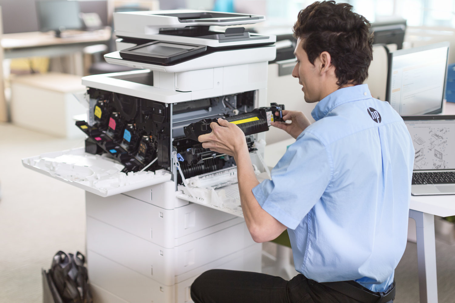 A printer technician with a manual open on a HP Elite x2 1012 G1 while replacing a part for a HP Color LaserJet Enterprise Flow MFP M577z.